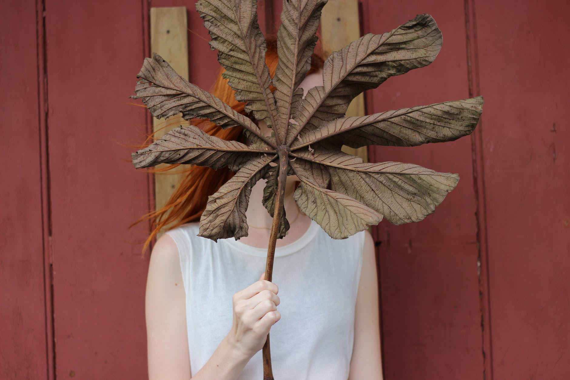 woman in white sleeveless shirt gold brown leaf in front of her face