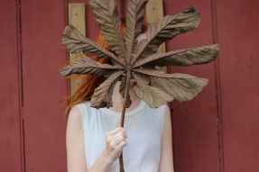 woman in white sleeveless shirt gold brown leaf in front of her face